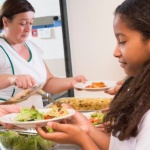 A girl is receiving a plate of food from a woman. 