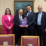 One woman and three men stood smiling with the middle two men holding a publication which reads - The road to net zero: renewables and nuclear working together