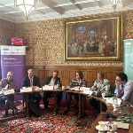 six academics sit at a roundtable behind a purple and white banner