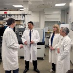 Four individuals are stood in a lab in discussion, wearing lab coats. 