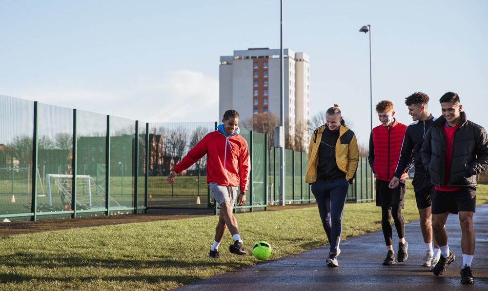 Teenage boys walking and playing with a football. 