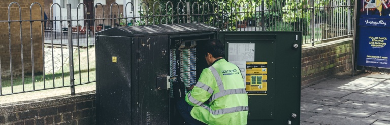 An image of a man kneeling down fixing a street level power box