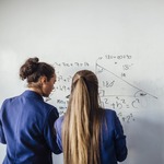 Two girls solving a math problem on a whiteboard