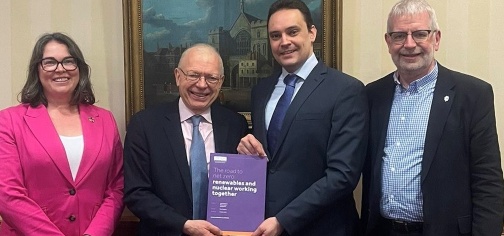 one woman and three men stood smiling with the two middle men holding a purple publication which reads "The road to net zero: renewables and nuclear working together"