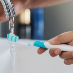 a toothbrush being rinsed from water running from a tap